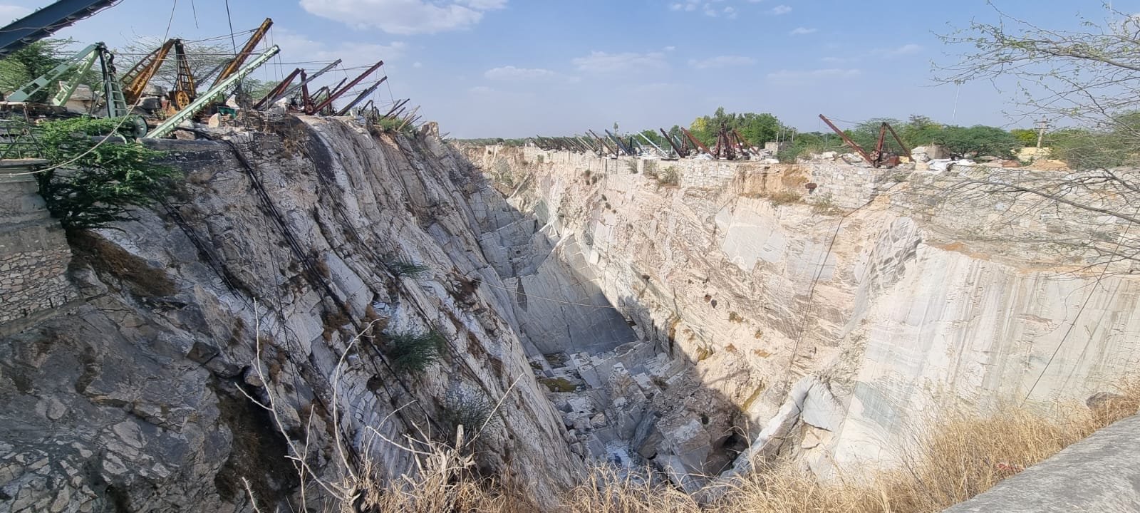 Deep open-pit mineral quarry with derrick cranes along the rim, Rajasthan